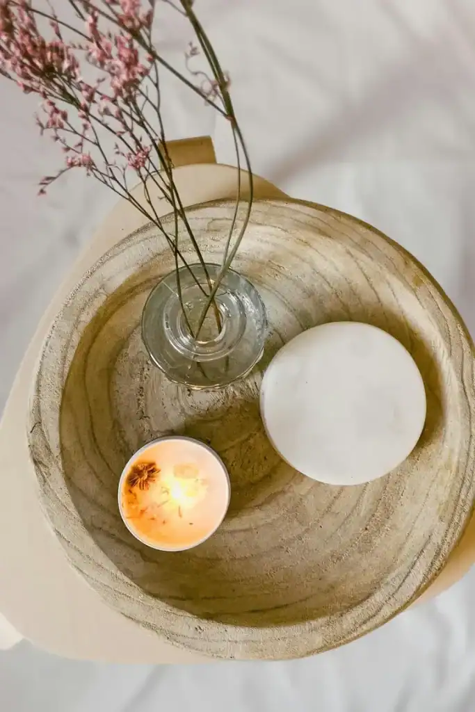 Minimalist decor with a vase of pink flowers, candle, and white sphere on wooden tray.